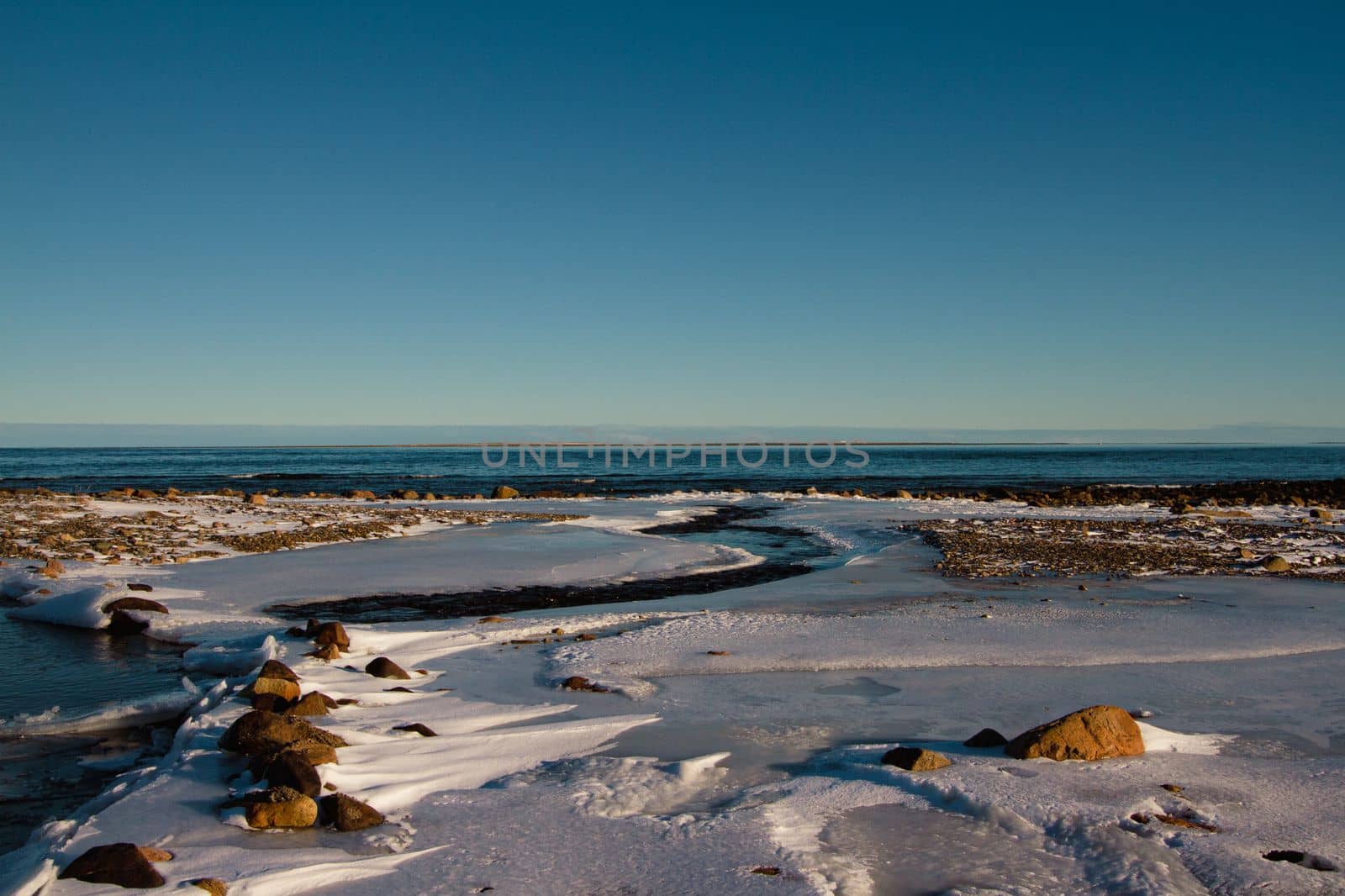 Arctic landscape - a small creek flowing into a larger waterbody surrounded by frozen arctic tundra with snow covered rocks by Granchinho