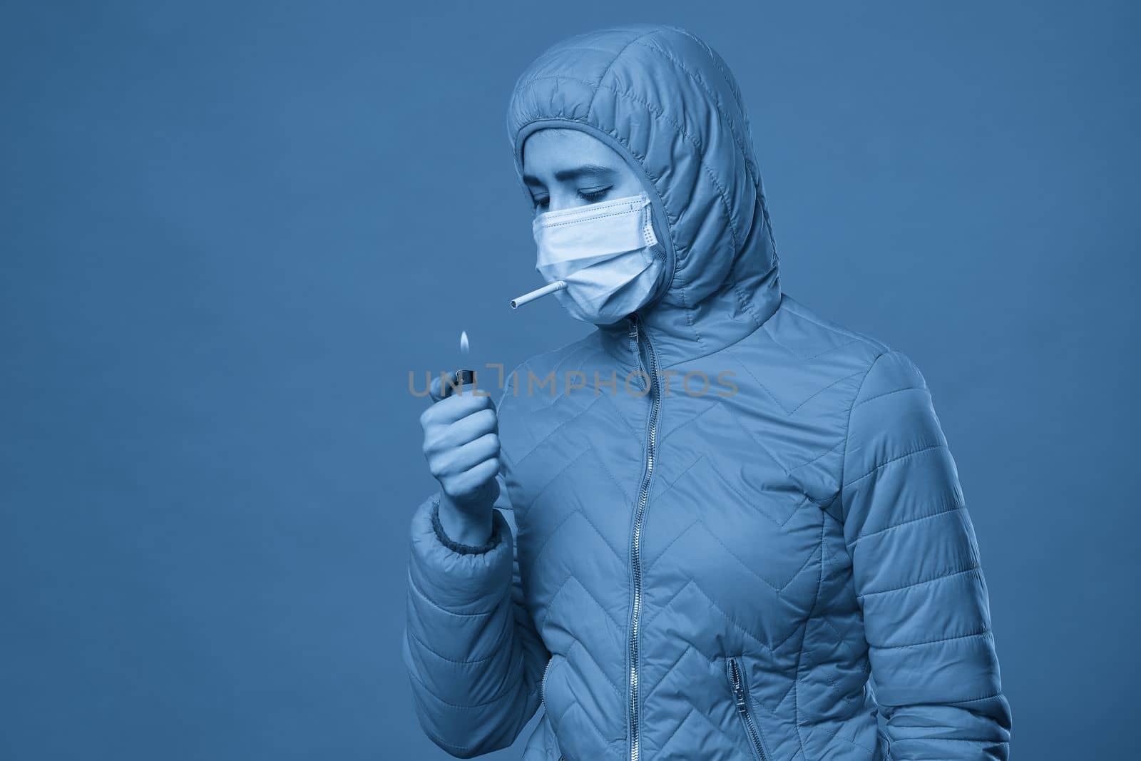 Young girl wearing medical protective mask lights up, holding a cigarette in her mouth through the mask. Copy space, close up