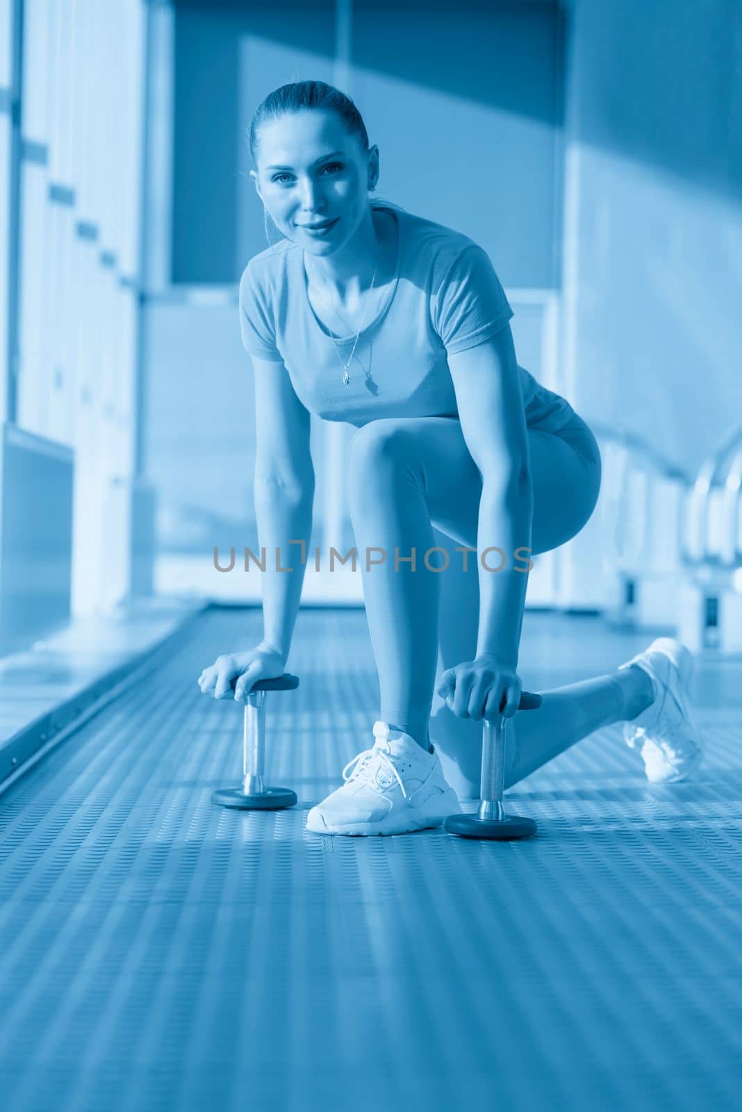 Physically fit woman at the gym lifting dumbbells to strengthen her arms and biceps. Muscular woman sitting on exercise mat looking at her arms.