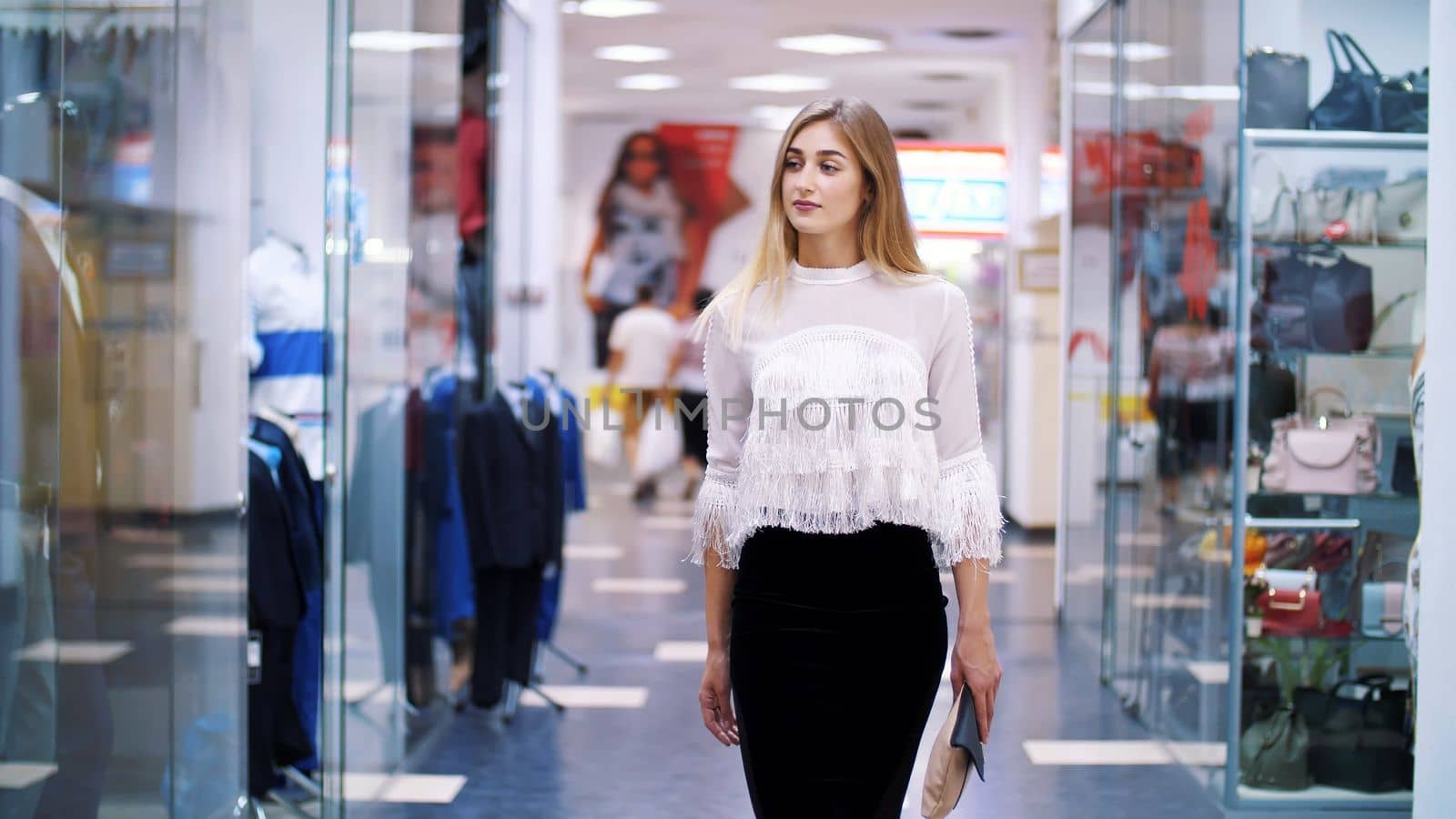 Sexy girl, tall, beautiful blond woman walking down the hall of shopping center, along the windows of shops and stylish boutiques. Shopping in a stylish clothing stores. High quality photo