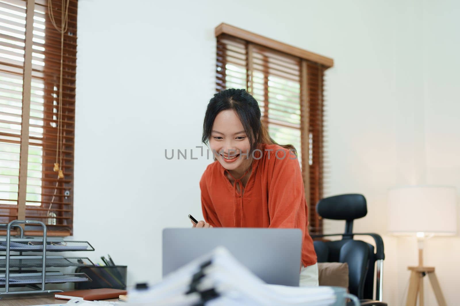 Portrait of a woman business owner showing a happy smiling face as he has successfully invested her business using computers and financial budget documents at work.