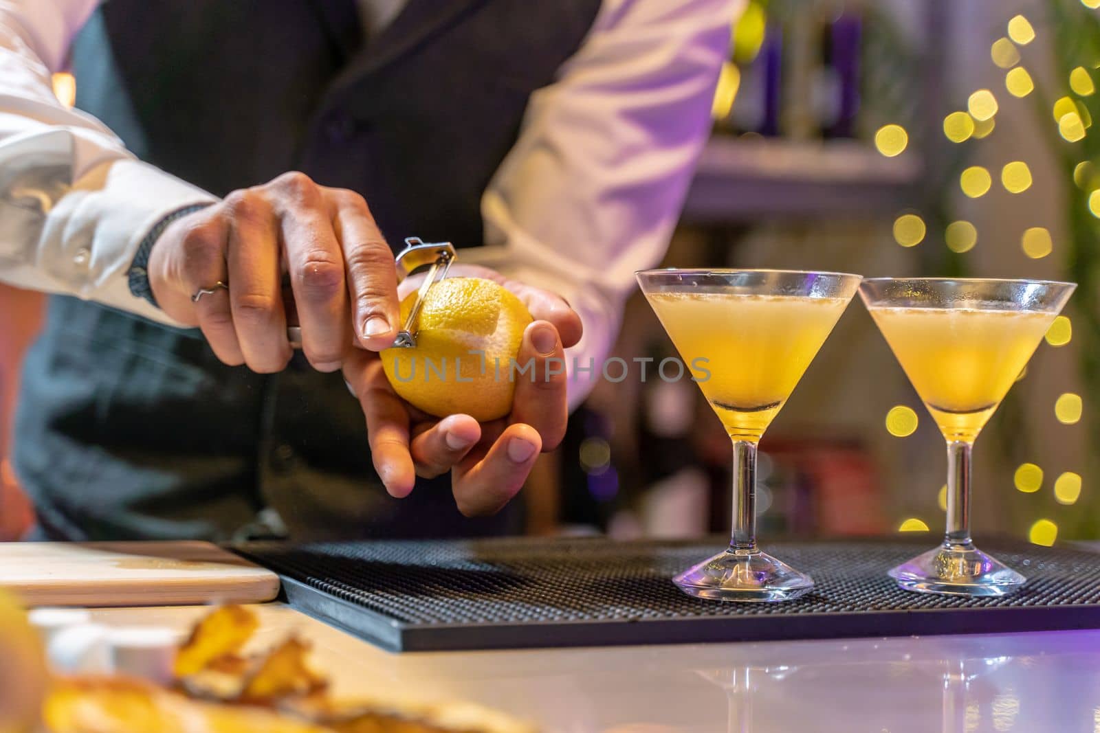 Closeup barman peeling lemon and making elegant cocktail in night club on bar counter with lights at nightclub party. High quality photo