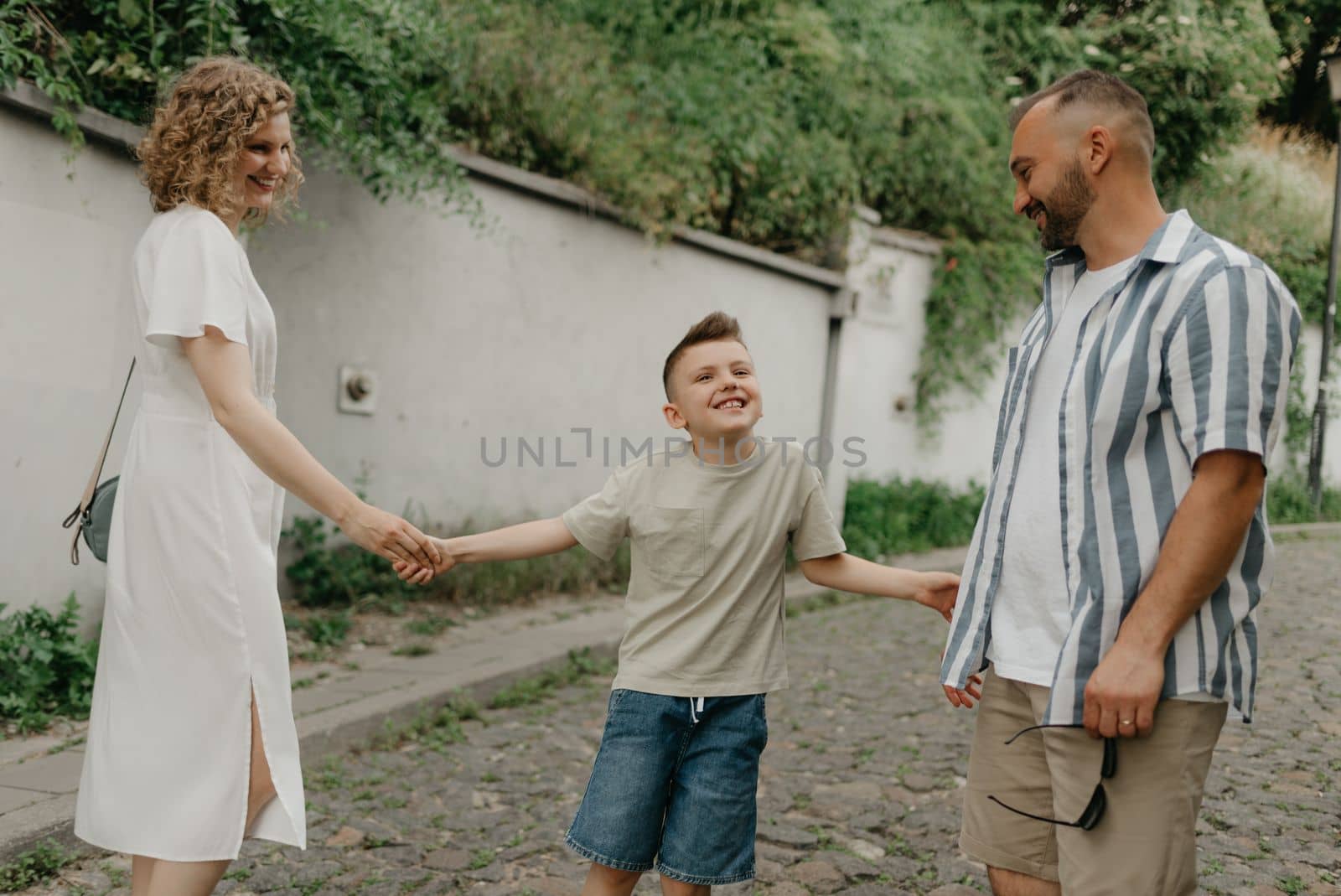 Father, mother, and smiling son are holding hands on the green cobbled street of an old European town. Happy family in the evening. Tourists at sunset.