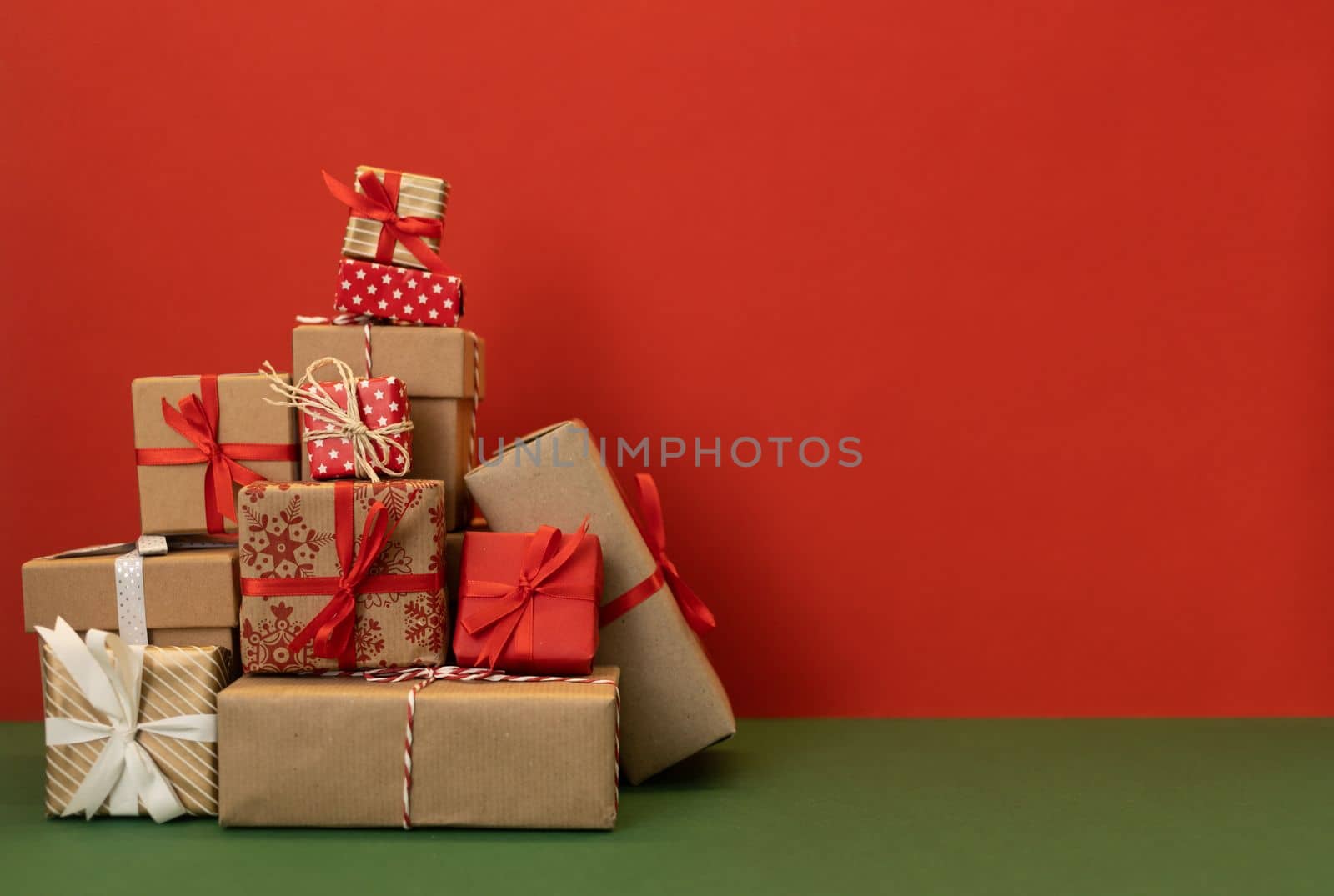 pile of craft wrapped christmas gifts on red background by Chechotkin