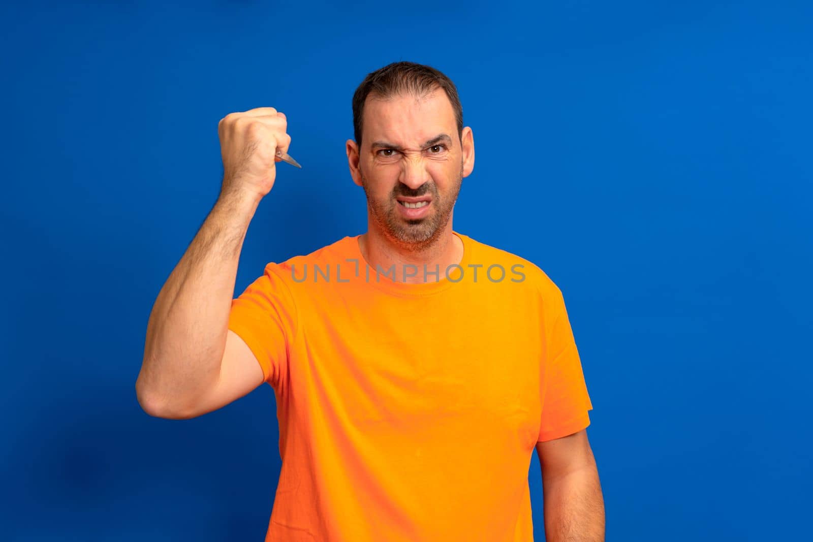 Hispanic man with beard holding scissors over isolated blue background annoyed and frustrated screaming with anger, crazy and yelling with raised hand, anger concept