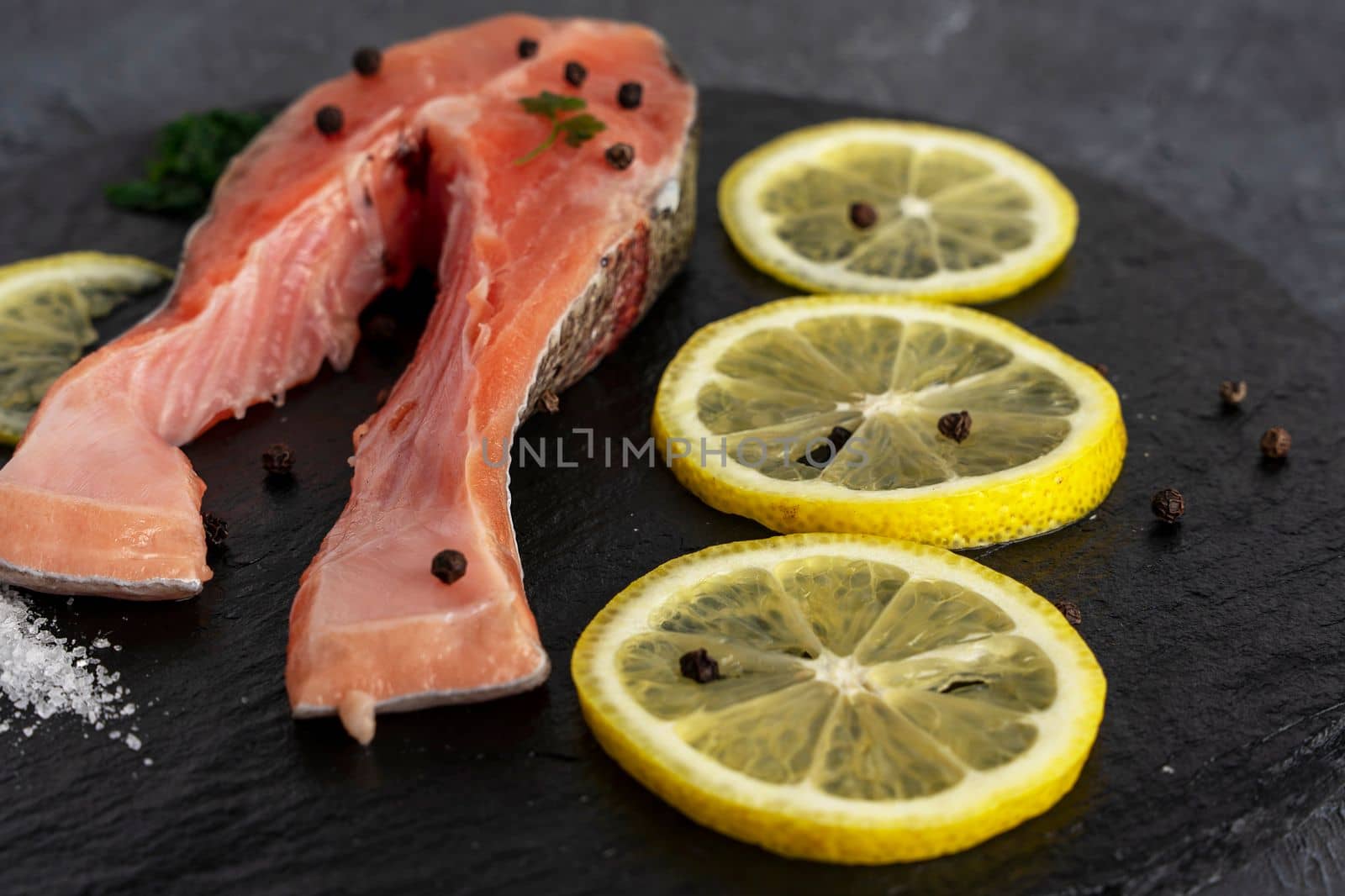 Fish steak with herbs, spices and lemon on a slate black board. Cooking fresh raw trout. Delicious juicy piece of trout for baking for dinner. High quality photo