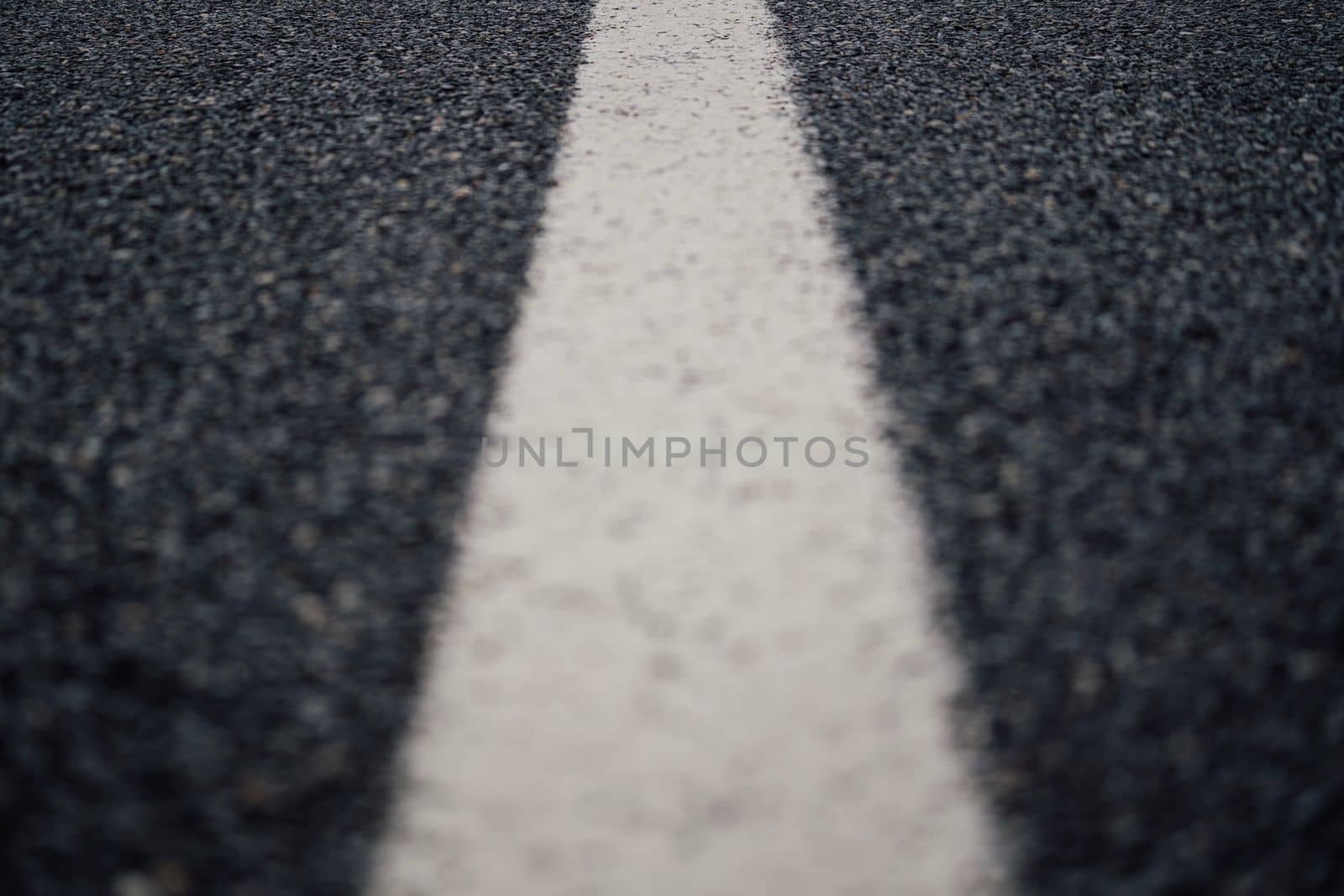 Low angle close-up of a white paint line on the center of a black asphalt road by papatonic