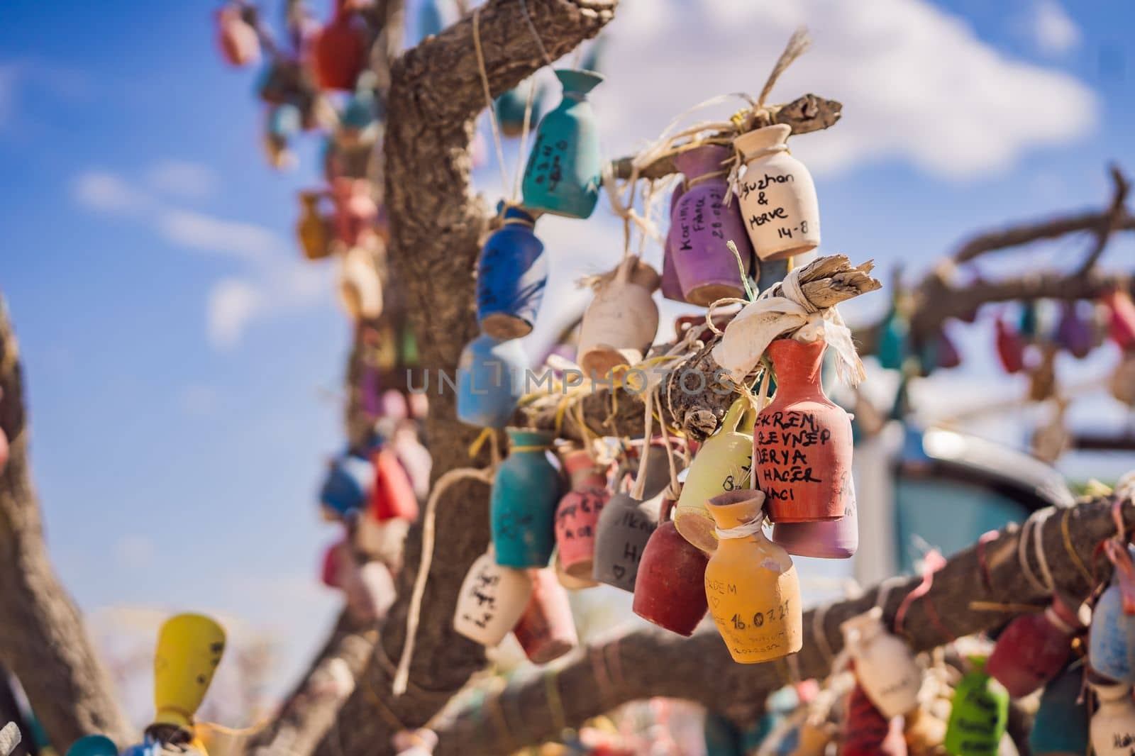 Wish tree. Small multi-colored jugs with inscriptions, wishes hanging on the branches of a tree., against the backdrop of sand ruins and blue sky.