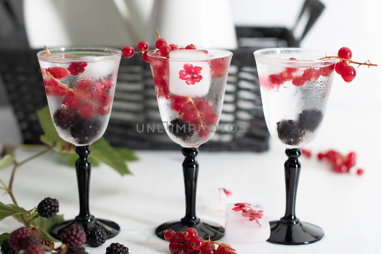 transparent gin and tonic with ice and fresh red currants and blackberries in beautiful crystal glasses against the background of a vase of flowers. High quality photo