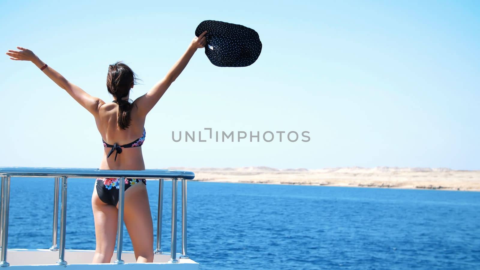 summer, sea, beautiful sexy young brunette woman, in a swimsuit and hat from the sun, stands on the deck of a ferry, ship, enjoys the beauty of the sea, mountain landscape. High quality photo