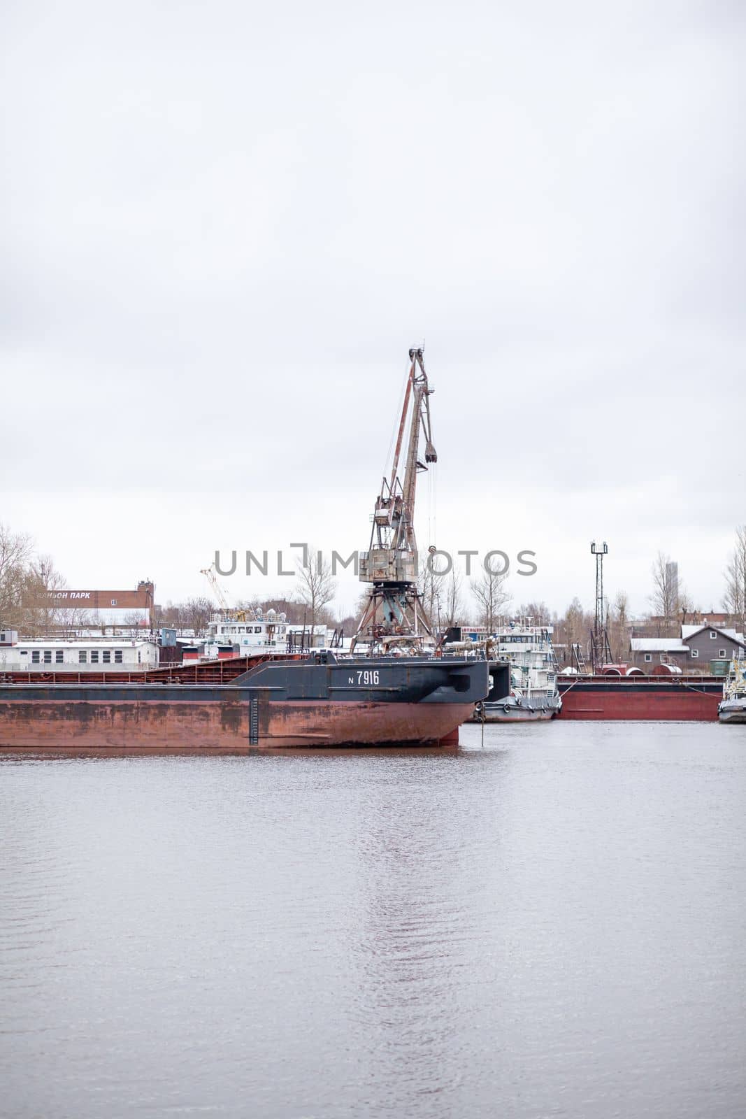 River port in winter. Port cranes on the bank of the river. Embankment of the river port, a barge at the quay wall. Large port cranes on the river. Extraction and transportation of sand other cargo