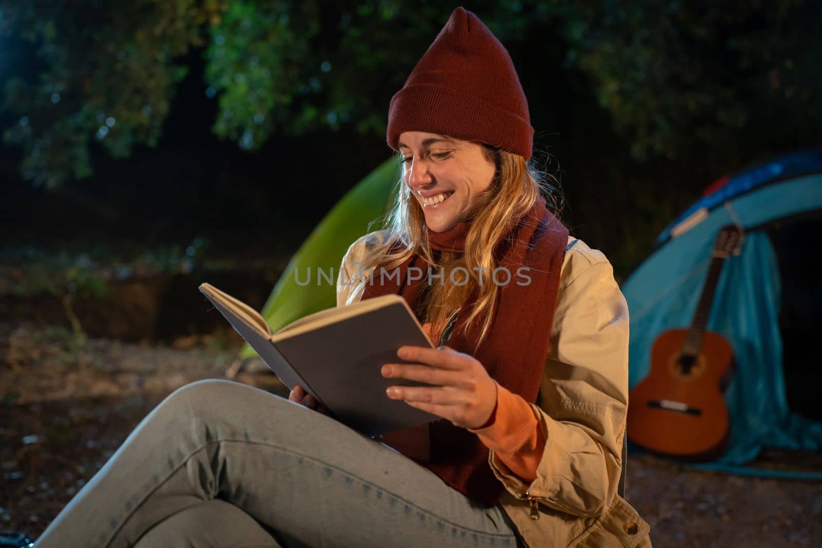 Girl reading a book at night camping. Night scene next to camping fire. Relaxing in quiet nature. High quality photo