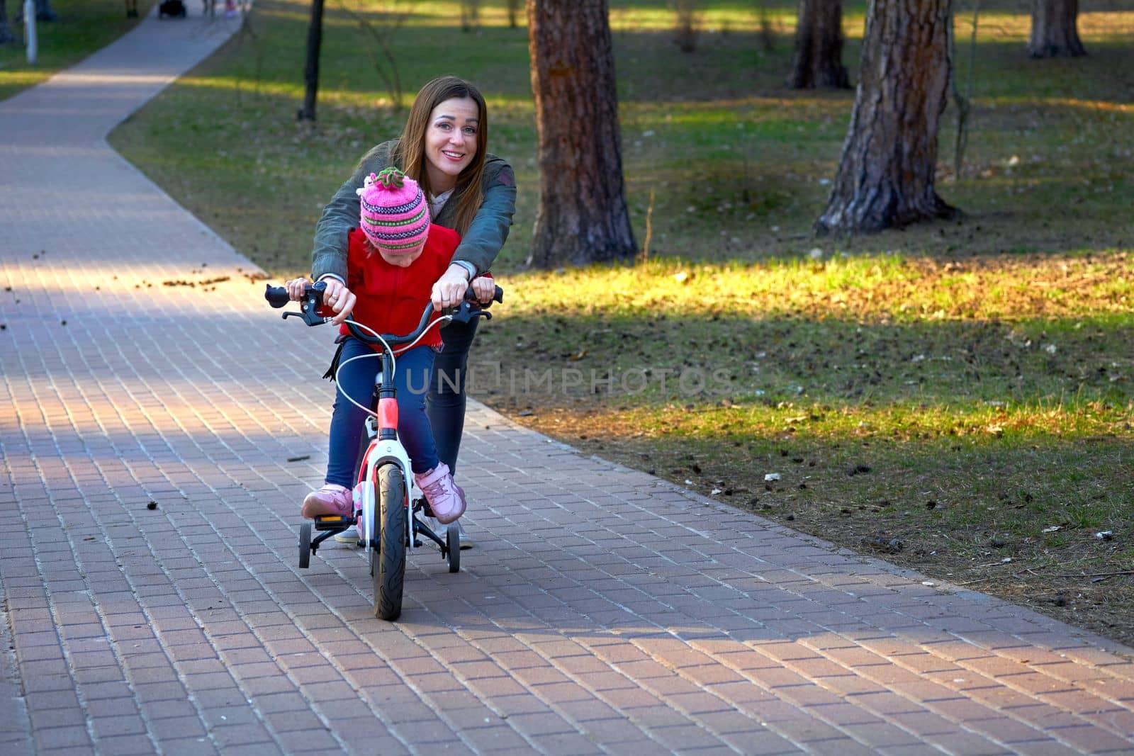 Cheerful mom teaches her child to ride a bike in autumn spring park by jovani68