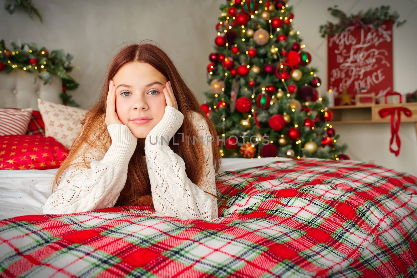 happy young teenage girl dreaming in bed over christmas tree lights on background. holidays and people concept.
