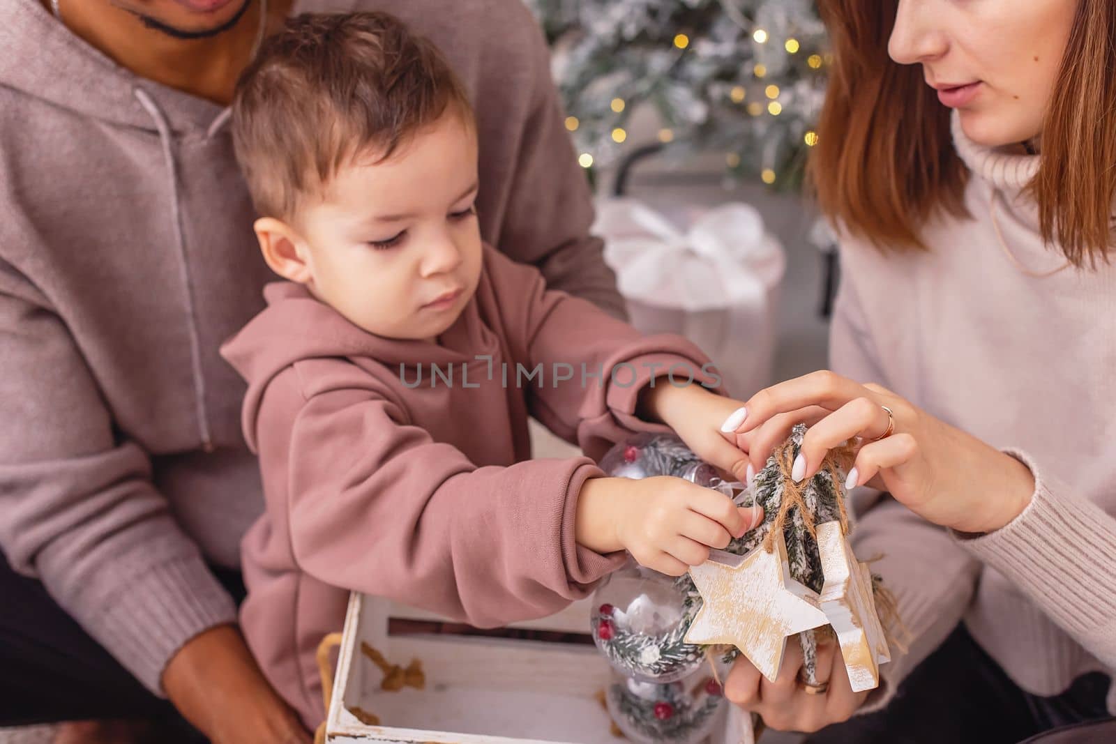 A little babyboy is sitting on his parents lap, taking wooden Christmas toys out of a wooden box. Close up