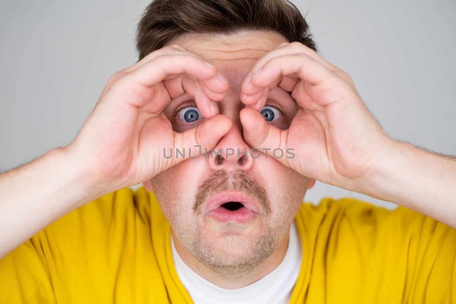 Caucasiann man making binoculars shape with his hands and looking through it. Eyesight problems