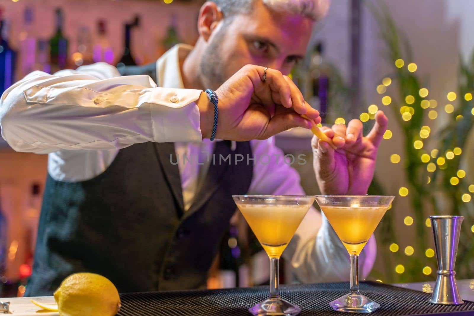 Handsome young barman making elegant cocktail in night club on bar counter with lights at nightclub party. High quality photo