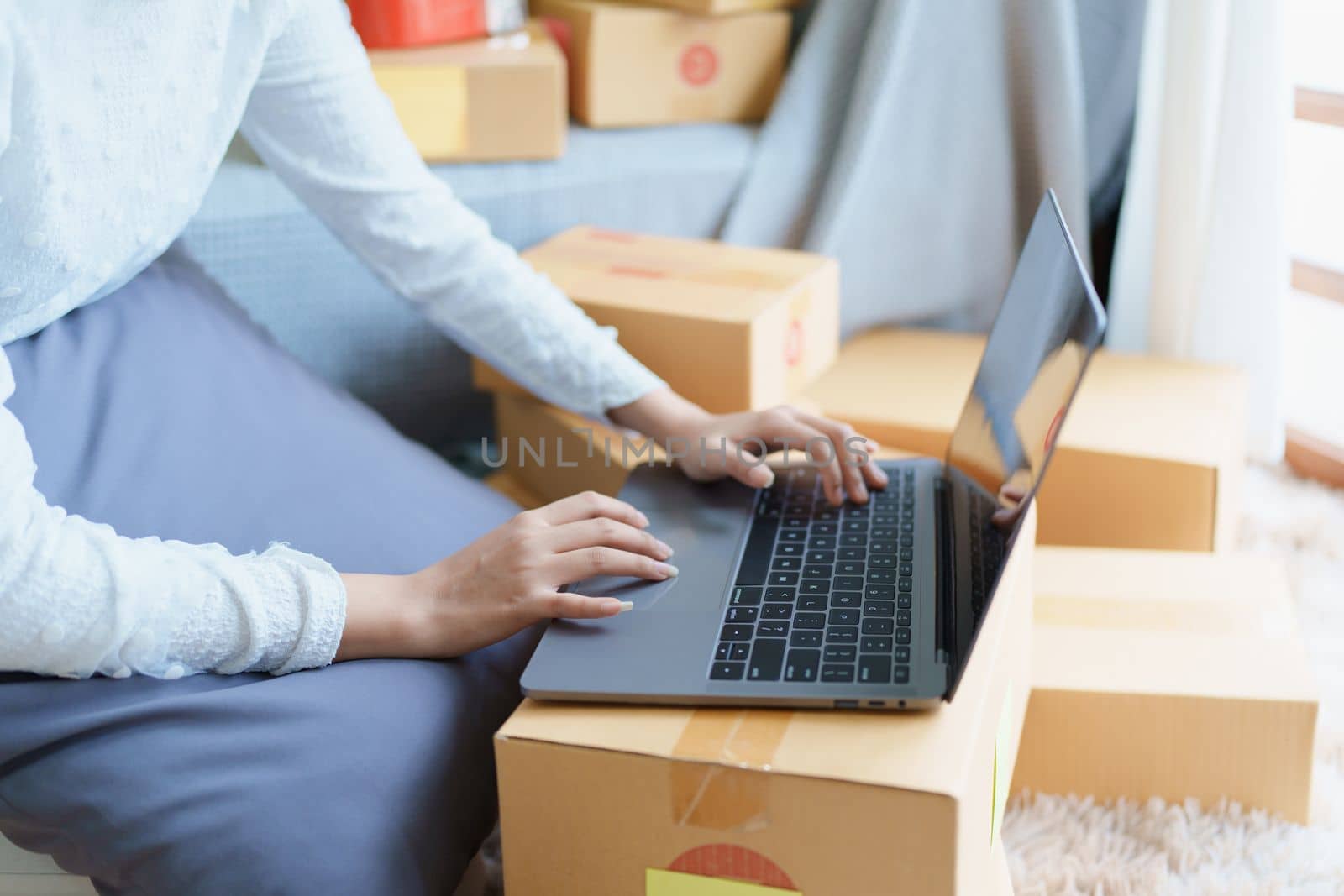 Starting small business entrepreneur of independent Asian woman smiling using computer laptop with cheerful success of online marketing package box items and SME delivery concept.