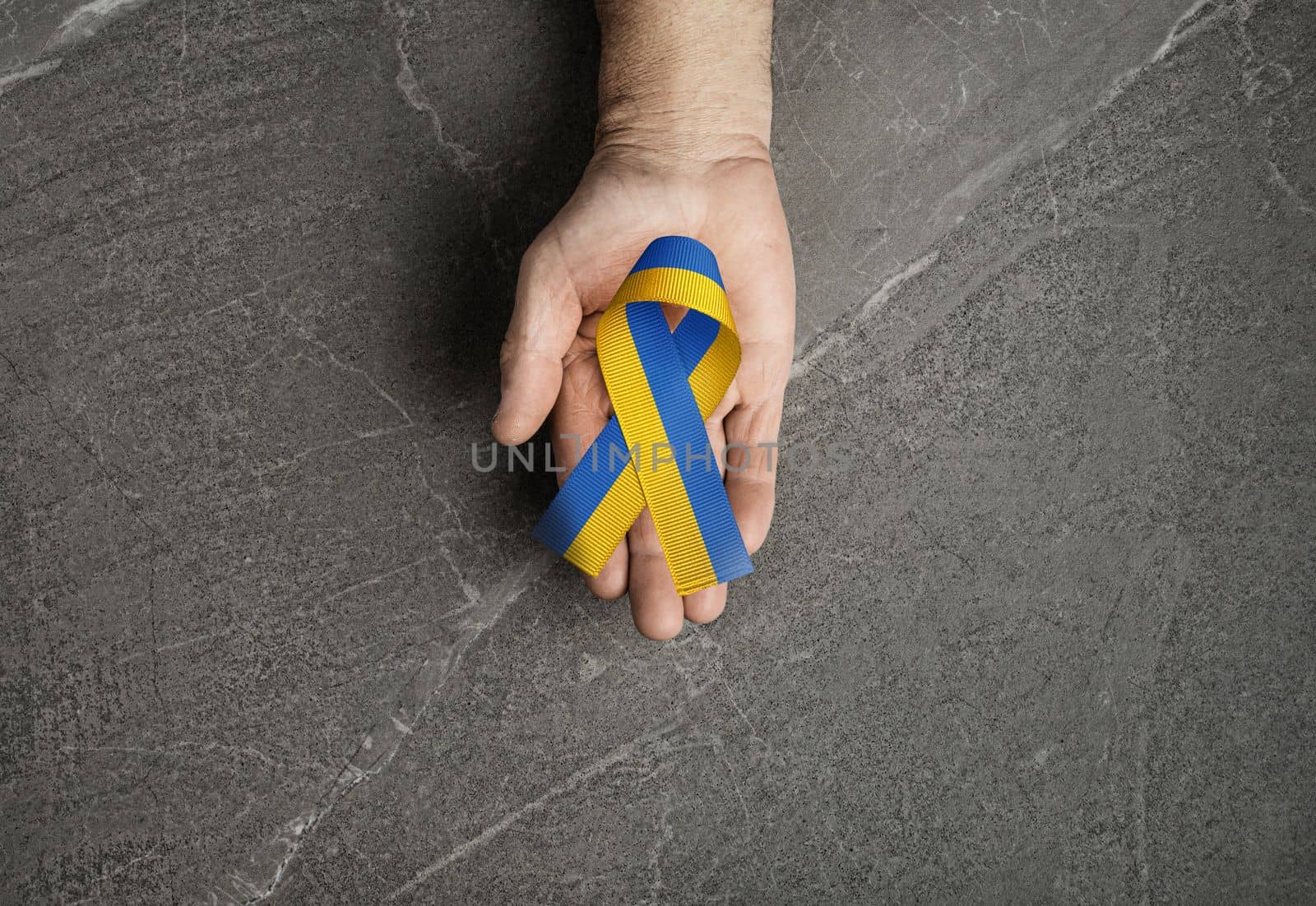 male hand with yellow and blue ribbon on marble background. concept needs help and support, truth will win