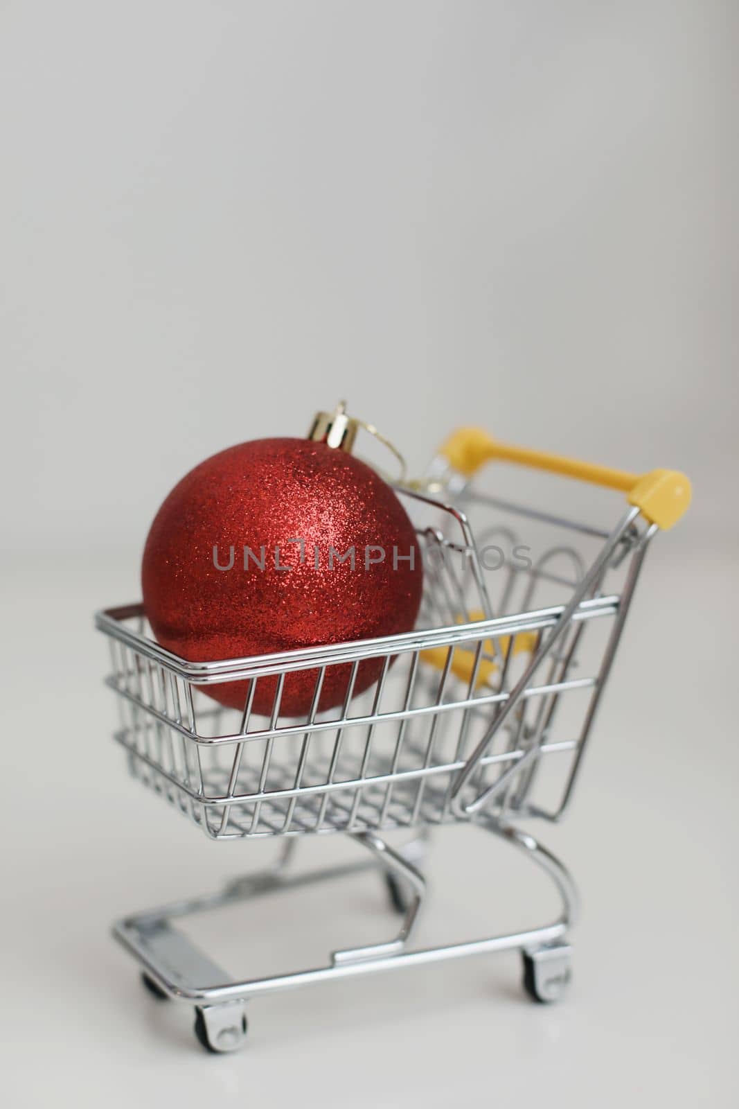 Small shopping cart with christmas ball on white background. Creative idea for shopping online, winter sale, supermarket, discount promotion and Black Friday concept. New Year and Christmas shopping