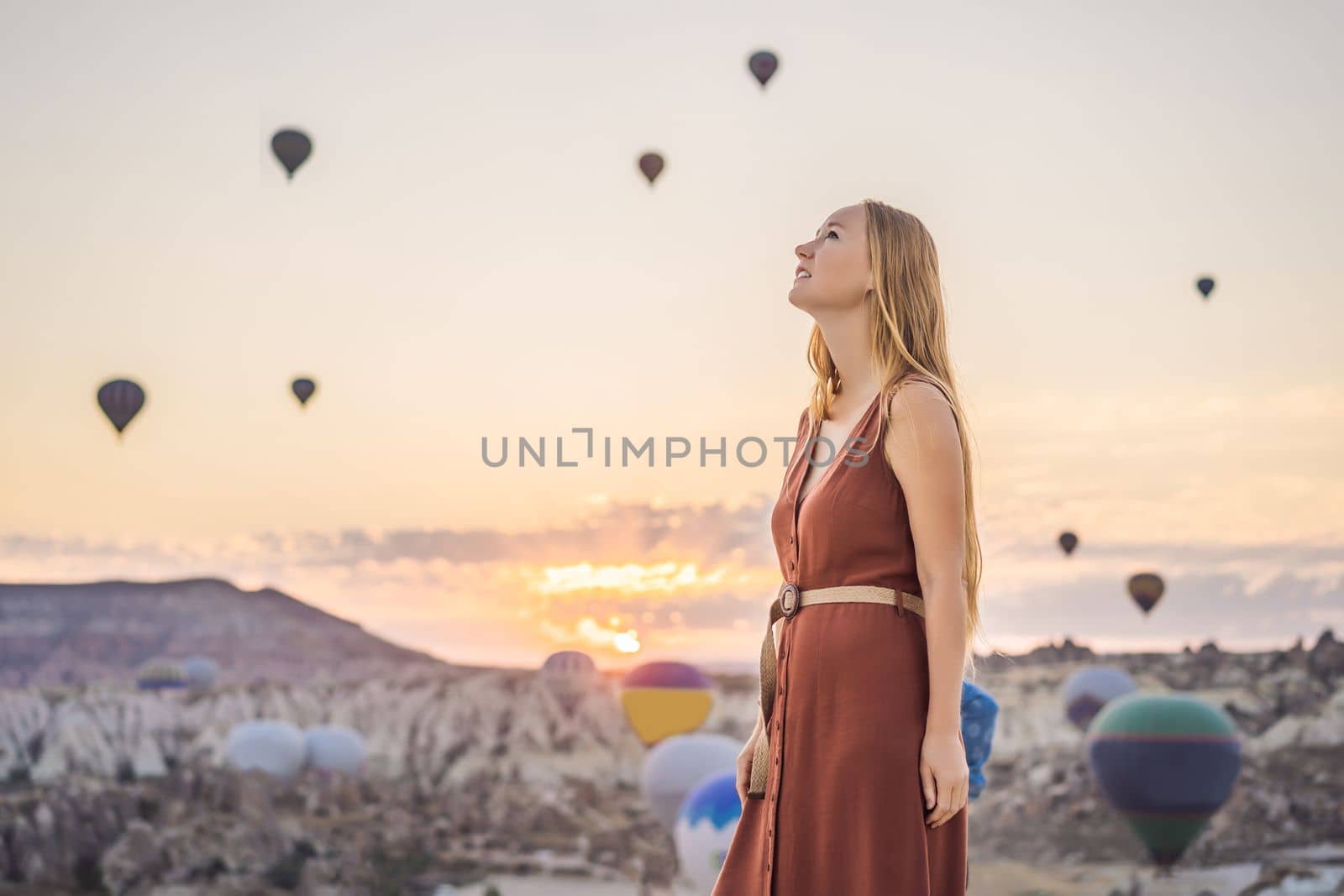 Tourist woman looking at hot air balloons in Cappadocia, Turkey. Happy Travel in Turkey concept. Woman on a mountain top enjoying wonderful view.