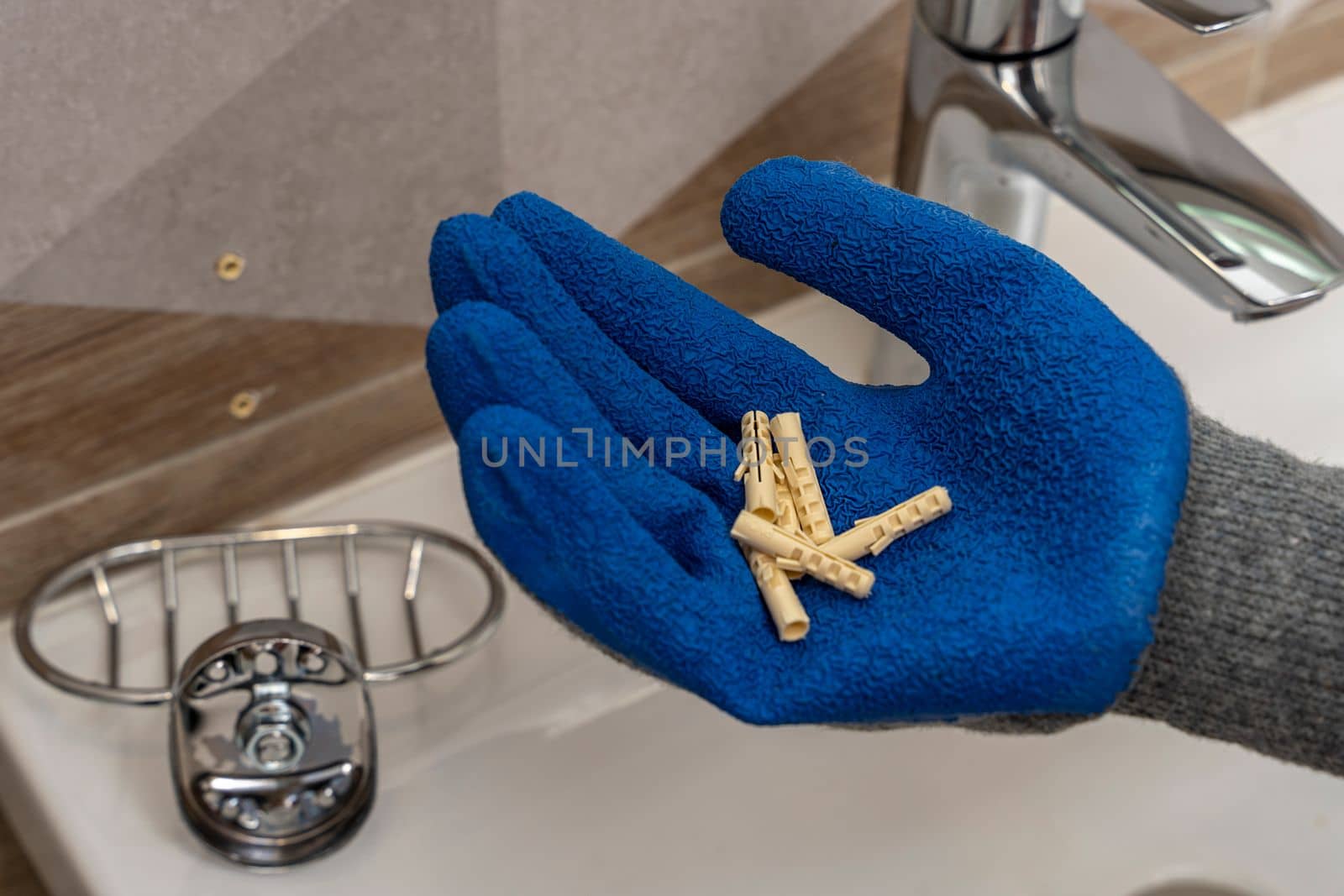 A worker's hand in protective gloves holds several plastic dowel pins in the palms against the background of the bathroom interior. renovation in the bathroom. installation of bathroom accessories.
