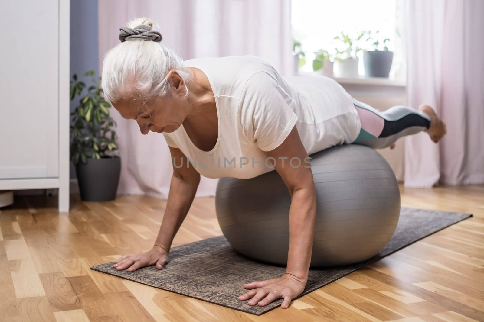 Middle aged woman in plank position keeps fit in her home. Elderly person has fun doing sports 