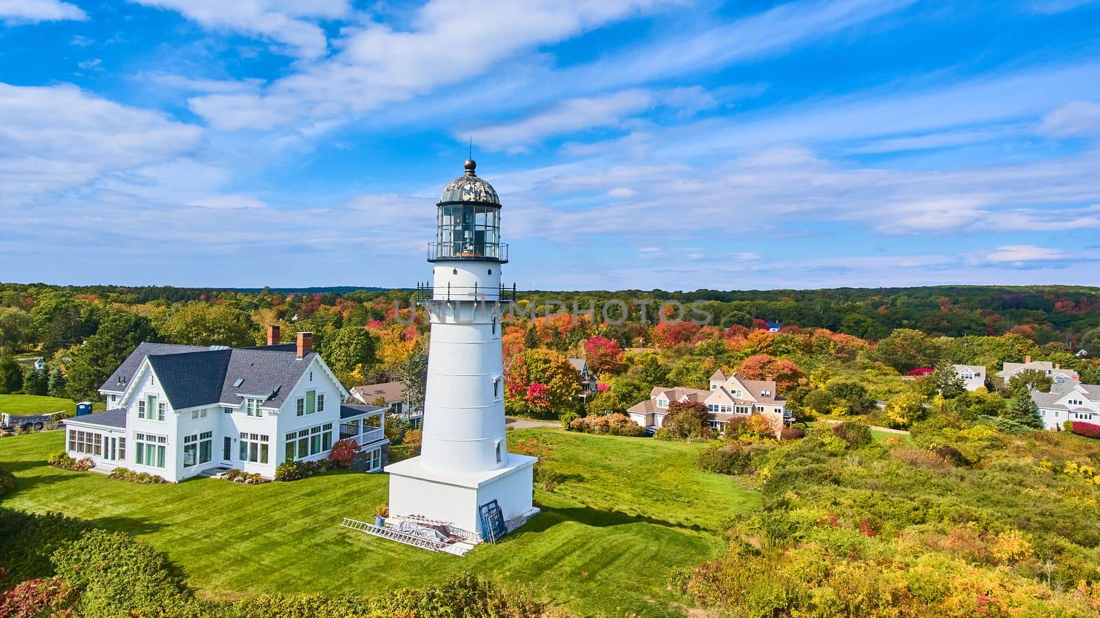 Single classic white lighthouse by homes with fall foliage around by njproductions