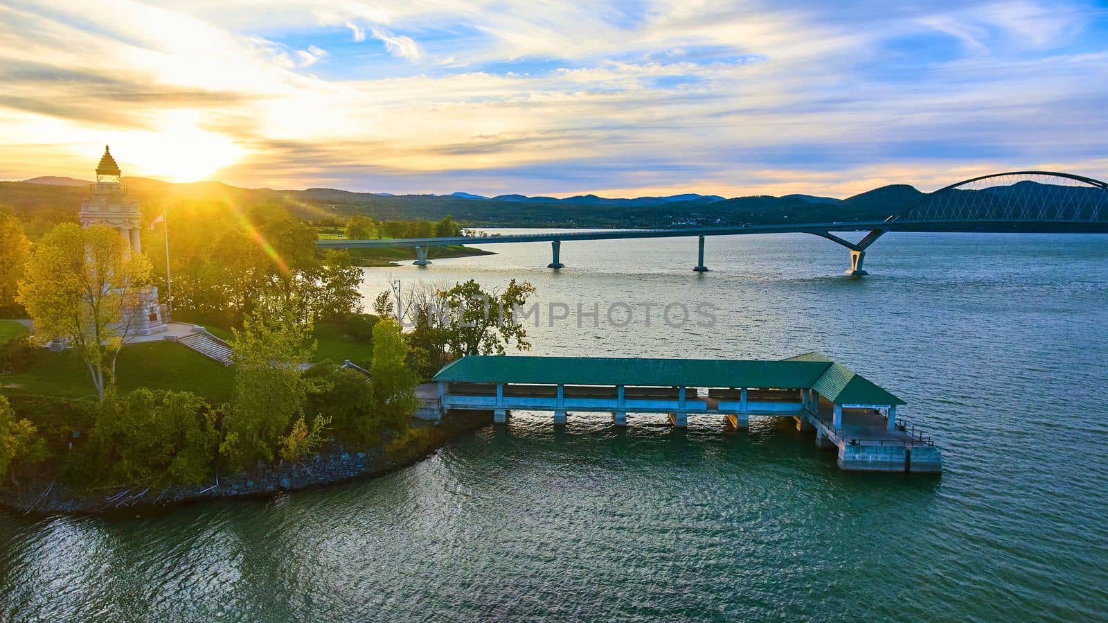 Image of Tower and docks with bridge connecting New York to Vermont and sun setting behind mountains