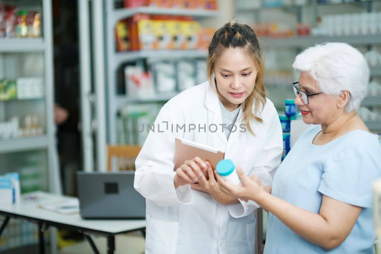 Young female pharmacist at the drugstore wearing white gown talking, giving advice, explaining, suggesting, and recommending to client or patient about the prescription and medications. Medicine and healthcare concept.