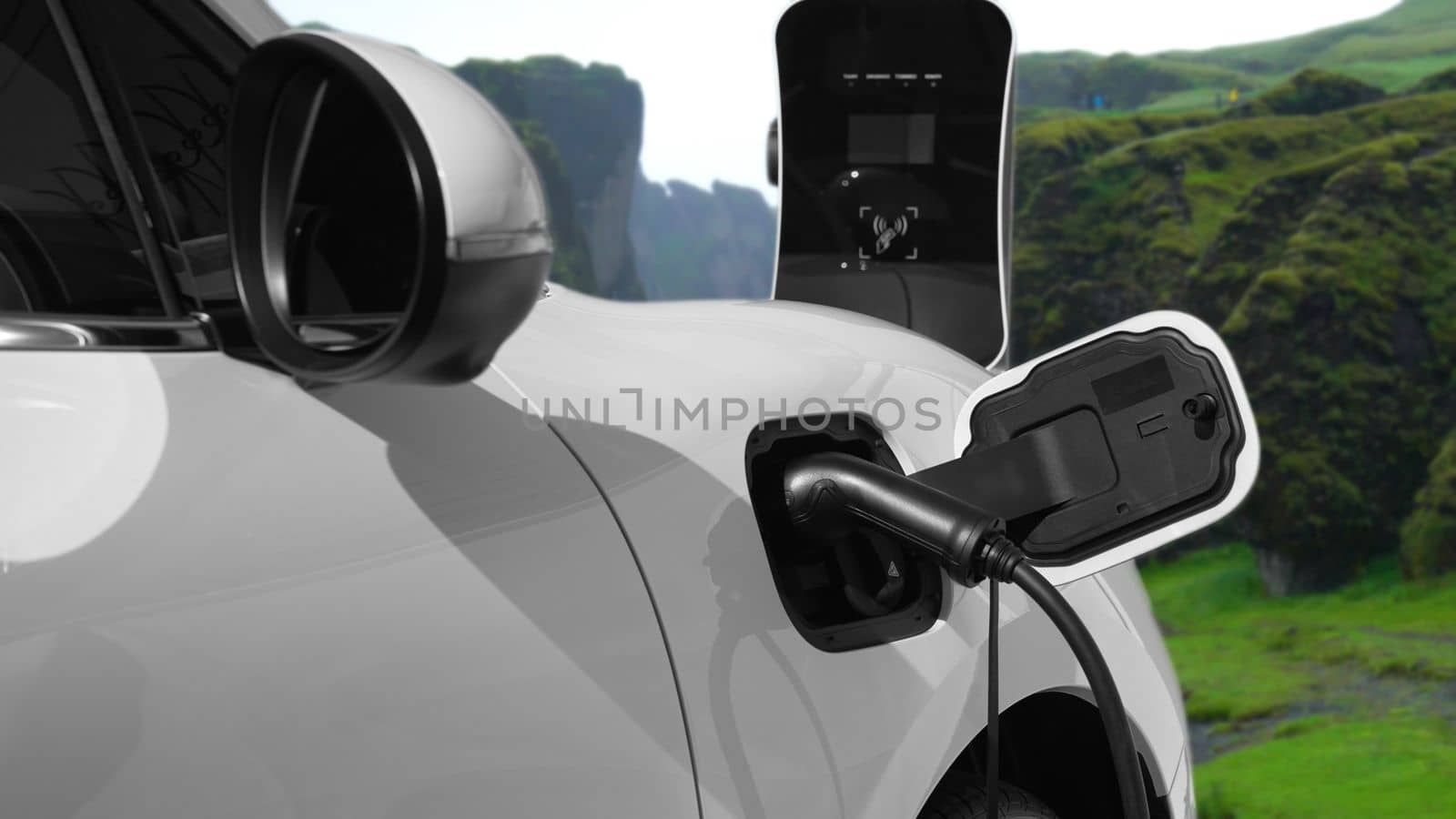 Energy sustainable car power by electro generator drive, recharge battery at charging station with mountain background for progressive travel concept. EV car in nature as symbol for clean environment.