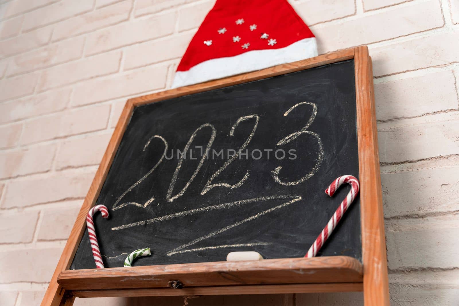 a black slate decorated with candy in the form of a caramel cane. The year 2023 is written in chalk on the blackboard. Happy New Year. 2023. Number written in chalk on a school board