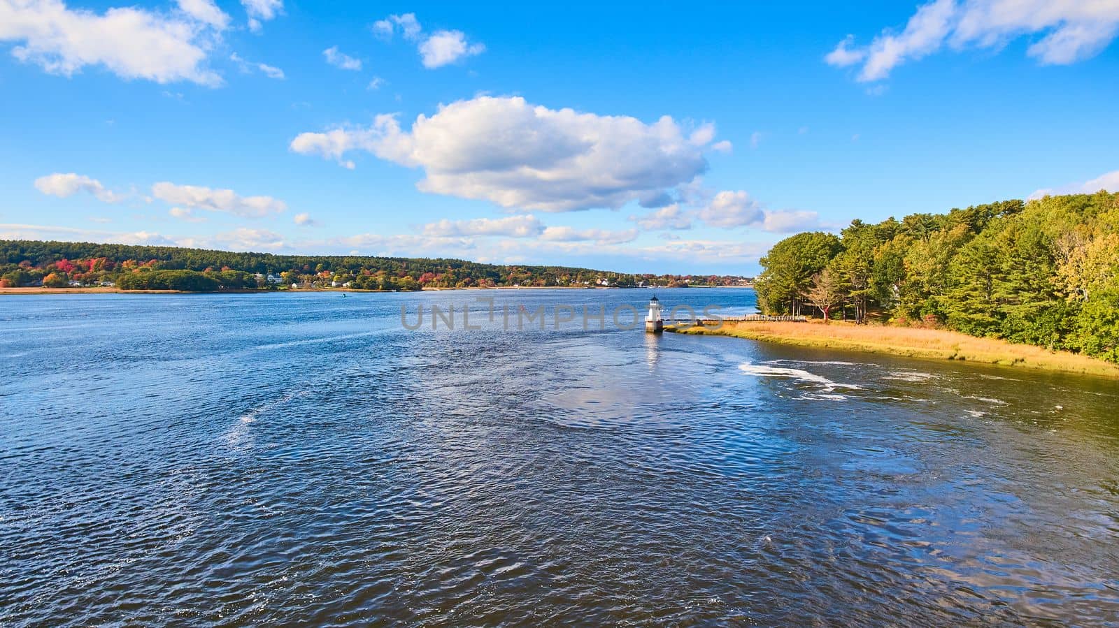 Image of Distant view over river of small lighthouse in Maine with fall foliage