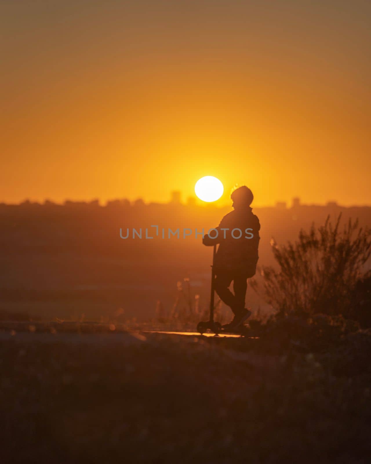 Boy silhouette on scooter against orange sunset warm sky with Madrid cityscape in the background. Sport, outdoor activity concept