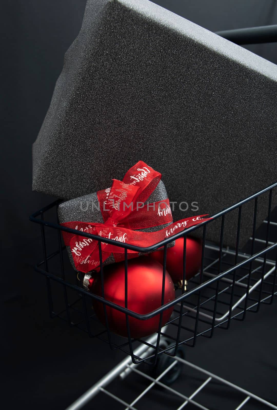 Christmas gift boxes in black paper in a shopping basket with red balls on a black background. High quality photo