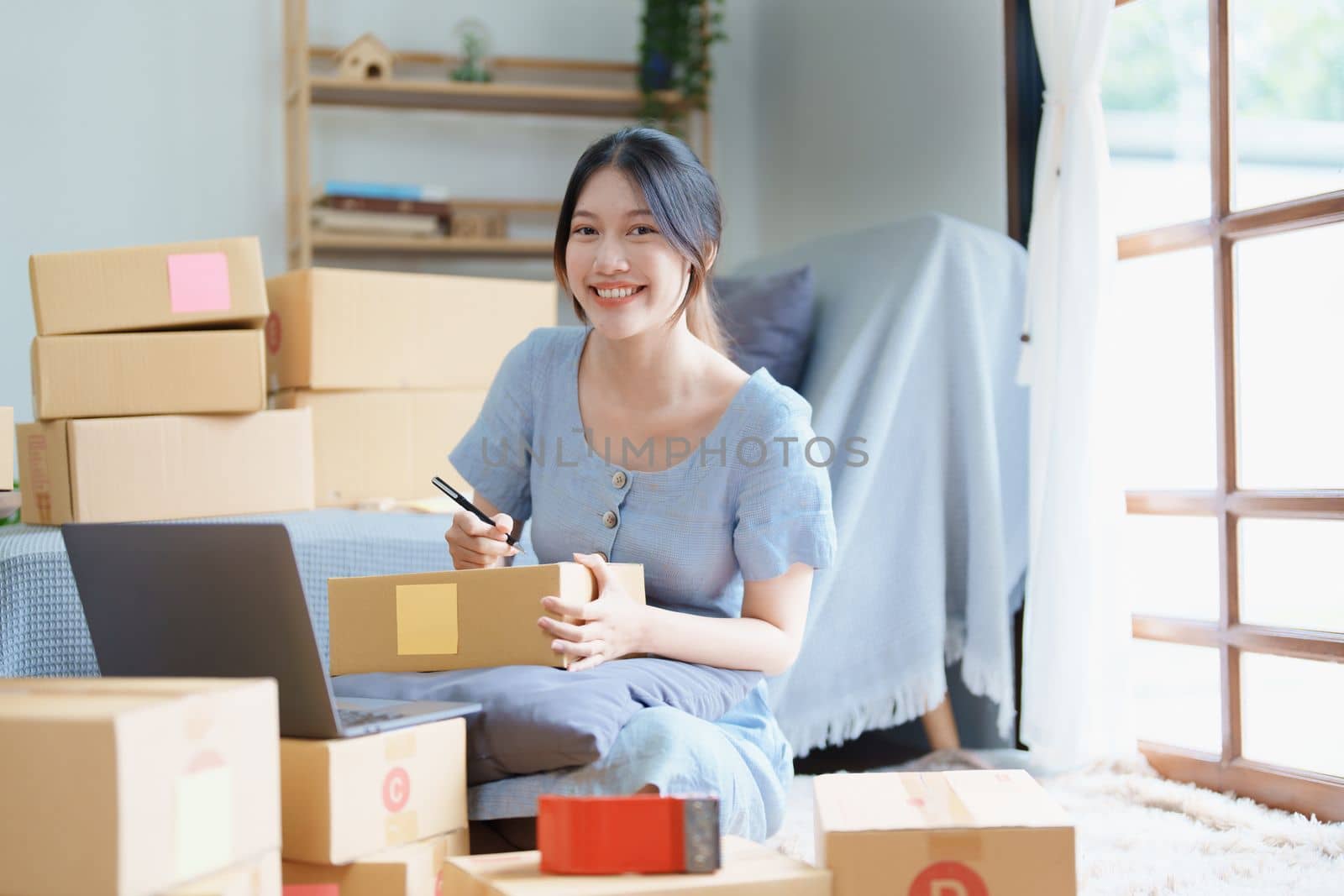 Starting small business entrepreneur of independent young Asian woman online seller is using computer and taking orders to pack products for delivery to customers. SME delivery concept by Manastrong