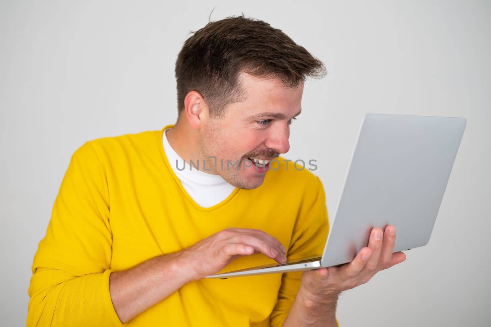Smiling attractive man holding laptop pc computer, surfing in internet by koldunov