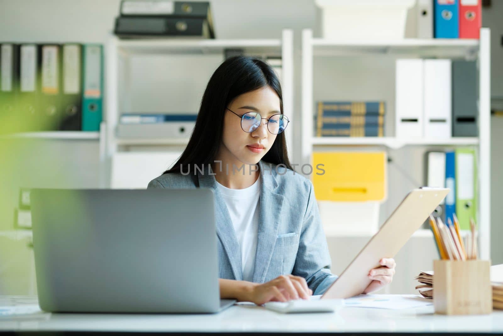 Young asian businesswoman working hard at the office using laptop data graphs, planning for improvement, analyzing and strategizing for business growth. Business concept