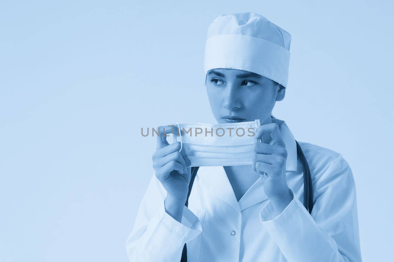 Portrait of young female doctor putting on protective medical face mask on white background, copy space by Mariakray