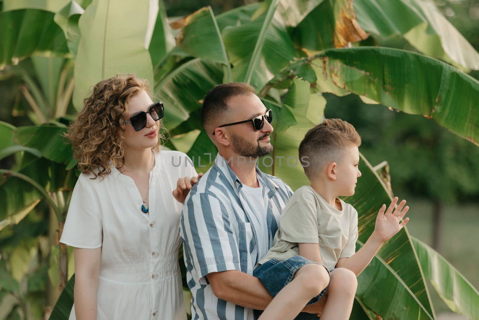Father, mother, and son are having fun with palm trees in the background. A close photo of a happy family in the garden in summer at sunset.