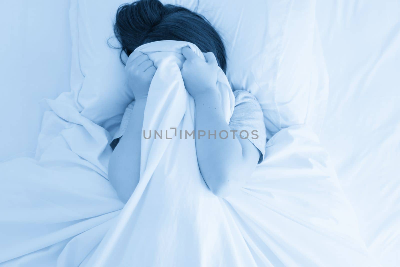 Woman hiding her face under a blanket in bed by Mariakray