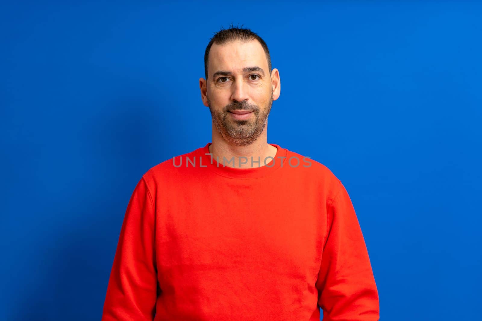 Spanish man with a beard posing happily for a half body portrait isolated on blue studio background