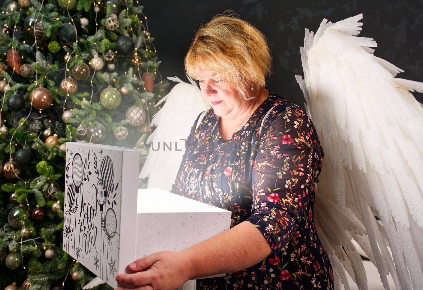 smiling lonely woman opens a christmas present near the christmas tree. Woman with angel wings, Christmas wonder.