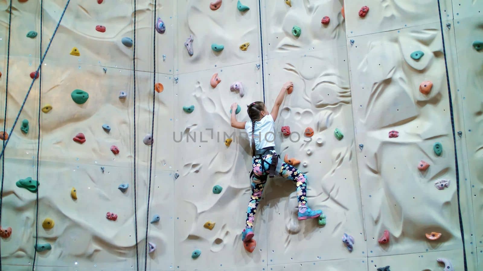 child climbs on a special wall for mountaineering. the girl of seven years in safety equipment is engaged in rock climbing on a special training vertical wall,. High quality photo