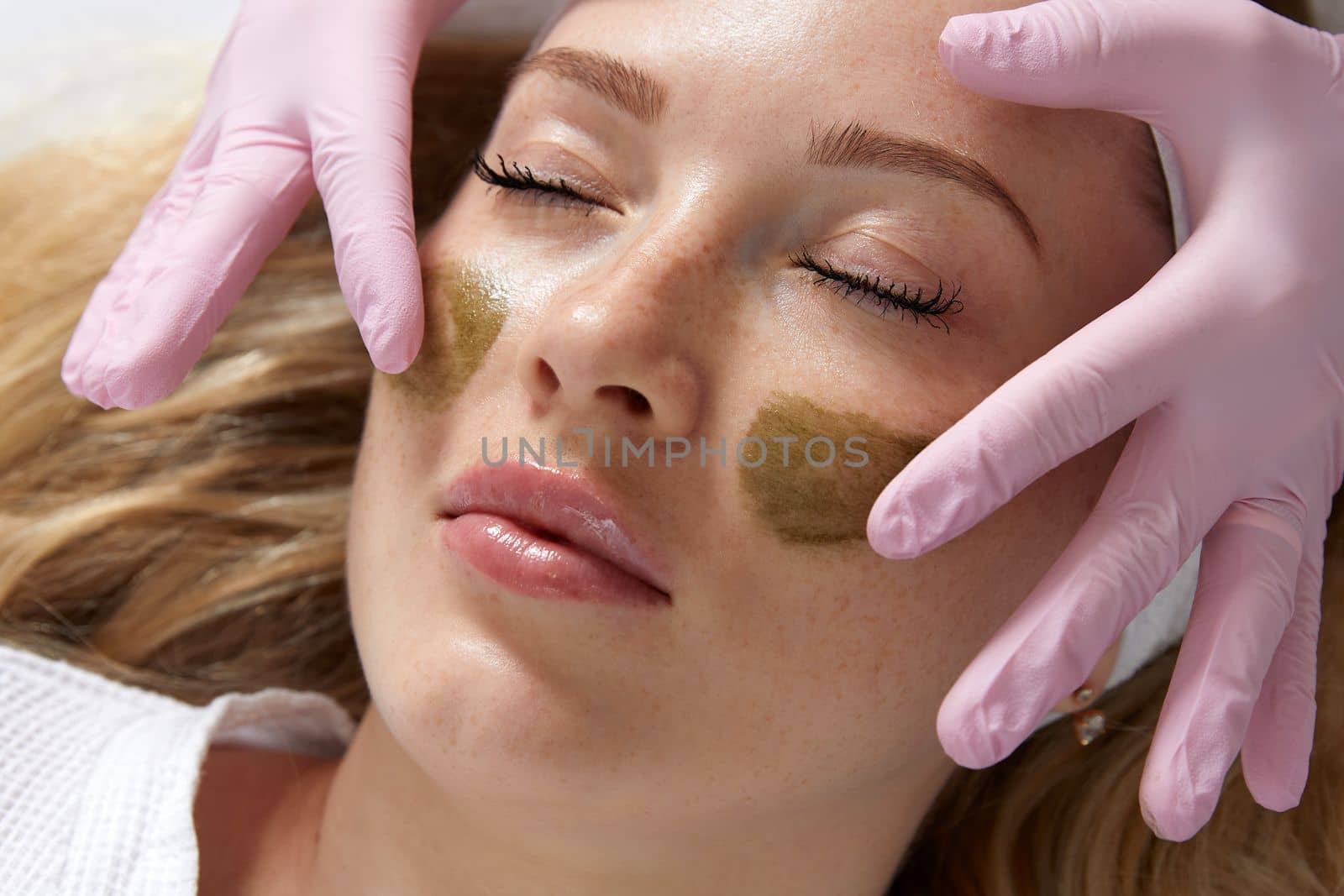 Cosmetologist applying a clay mask to the face of beautiful woman. Spa treatment in the beauty salon