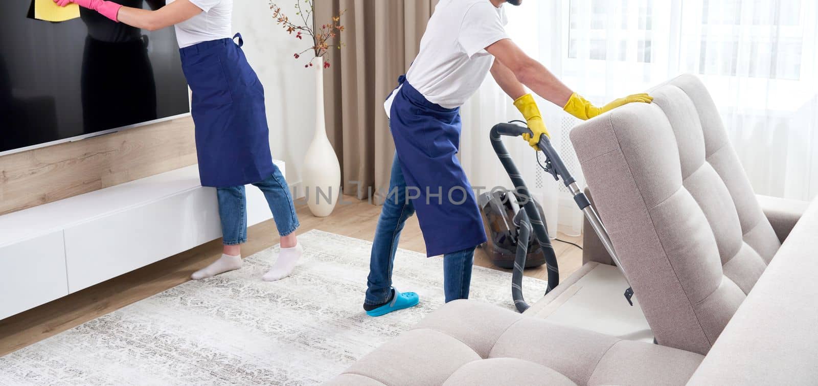 Professional cleaners washing floor and wiping dust from the furniture in the living room of the apartment. Cleaning service concept