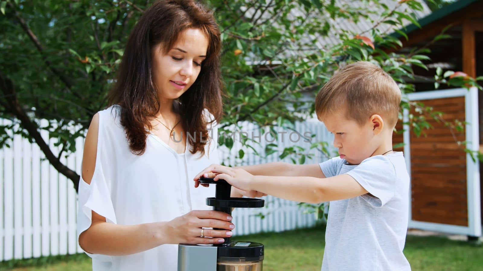 summer, in the garden. mother and four-year-old son make fresh juice of mandarins, put mandarin slices in a juicer. High quality photo