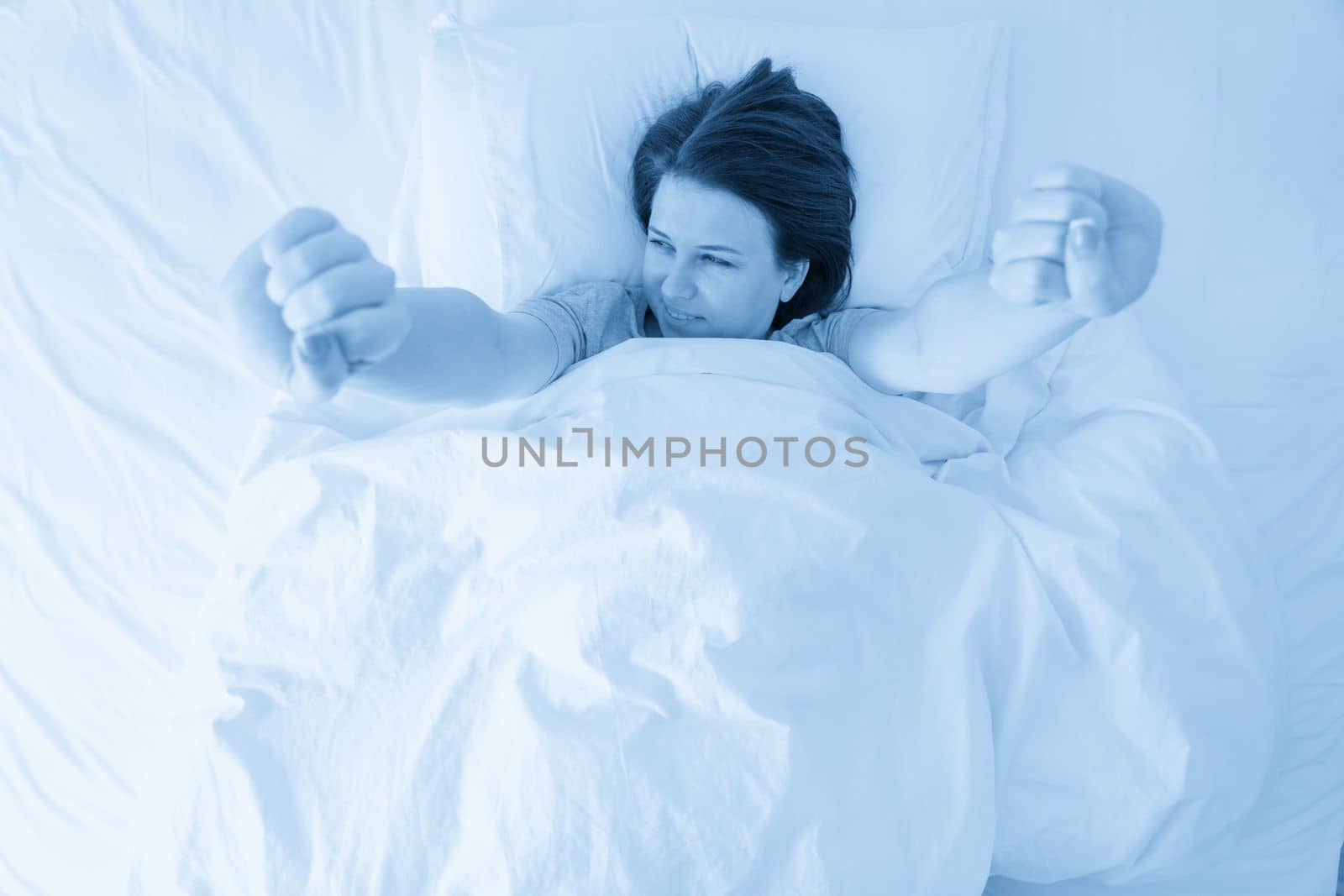 Portrait of young beautiful woman in bed stretching in the morning by Mariakray