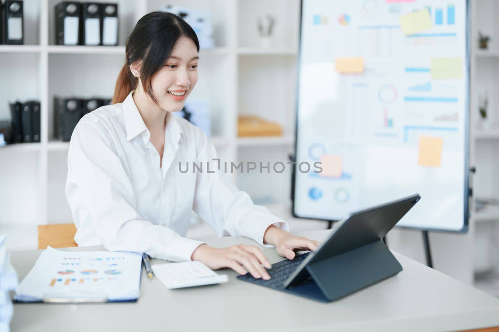 Portrait of a thoughtful Asian businesswoman looking at financial statements and making marketing plans using a computer on her desk.