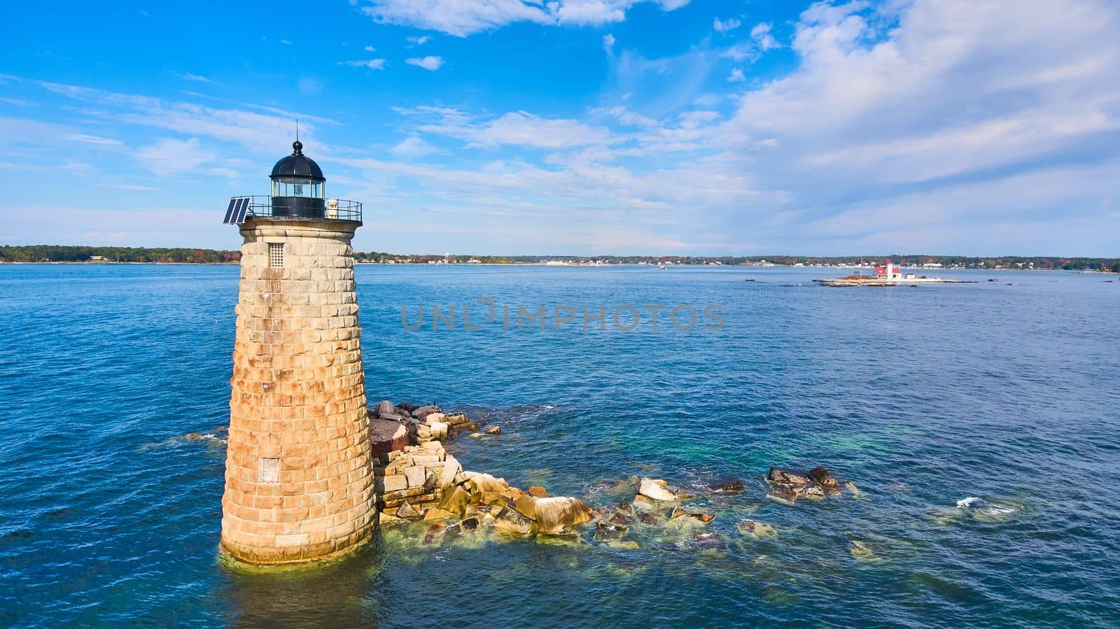 Lone stone tower lighthouse on broken rocks in Maine ocean by njproductions